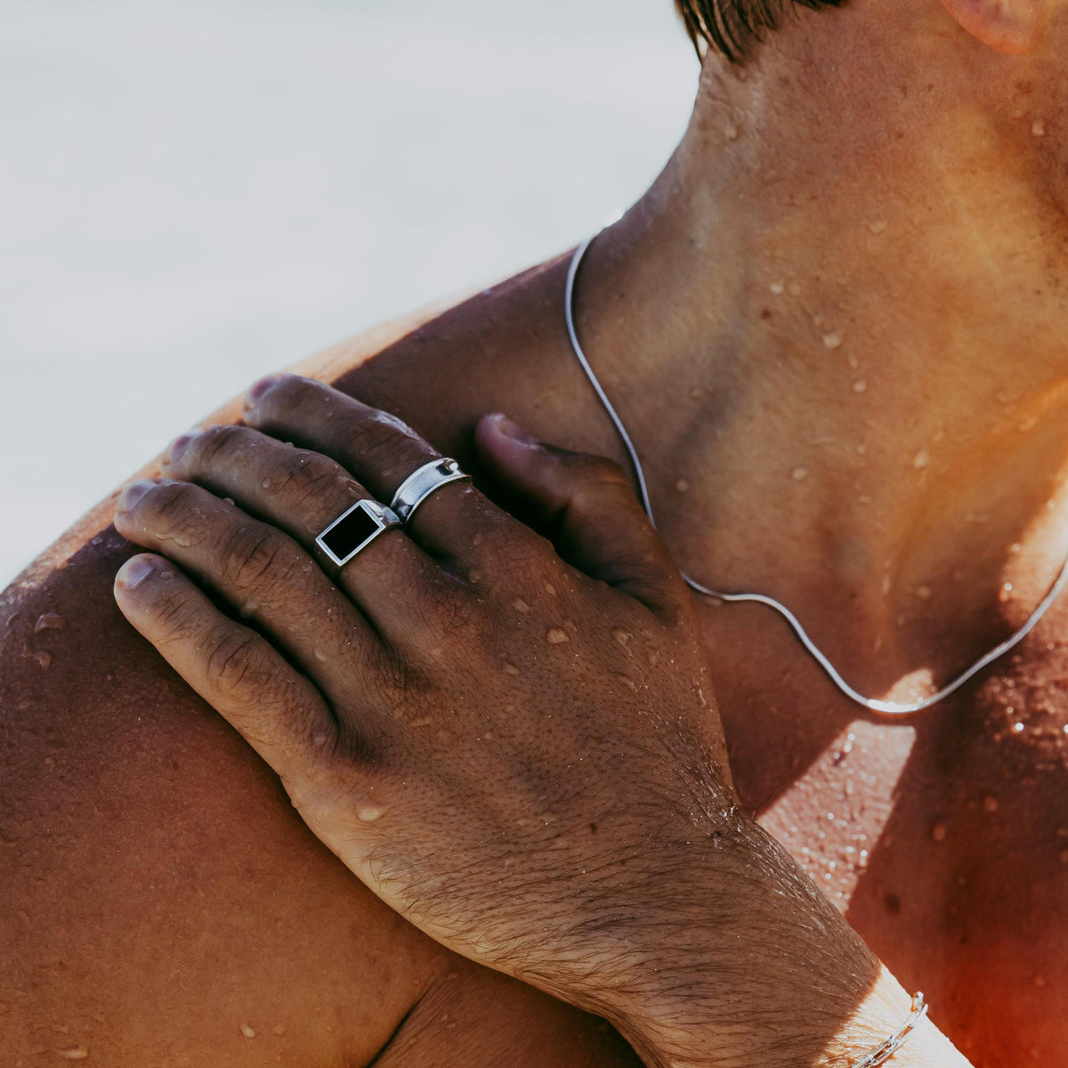 Close-up of a man's hand on his shoulder, wearing the Billie Jo Link Bracelet and rings. The sterling silver jewellery contrasts with his sun-kissed skin, capturing a modern, masculine, and editorial vibe for the Australian brand.