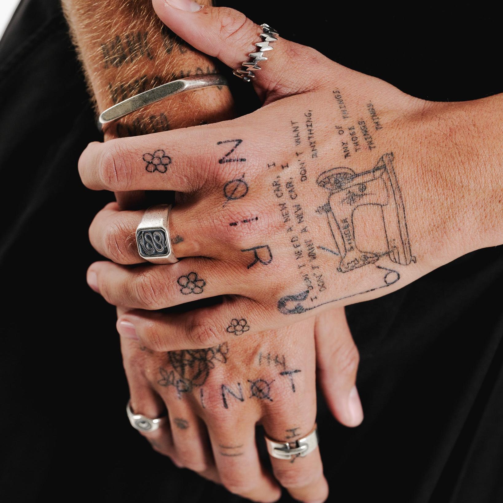 A tattooed hand wearing the sterling silver Surge Ring from Billie Jo. The ring's sharp, modern design contrasts with the dark tattoos.