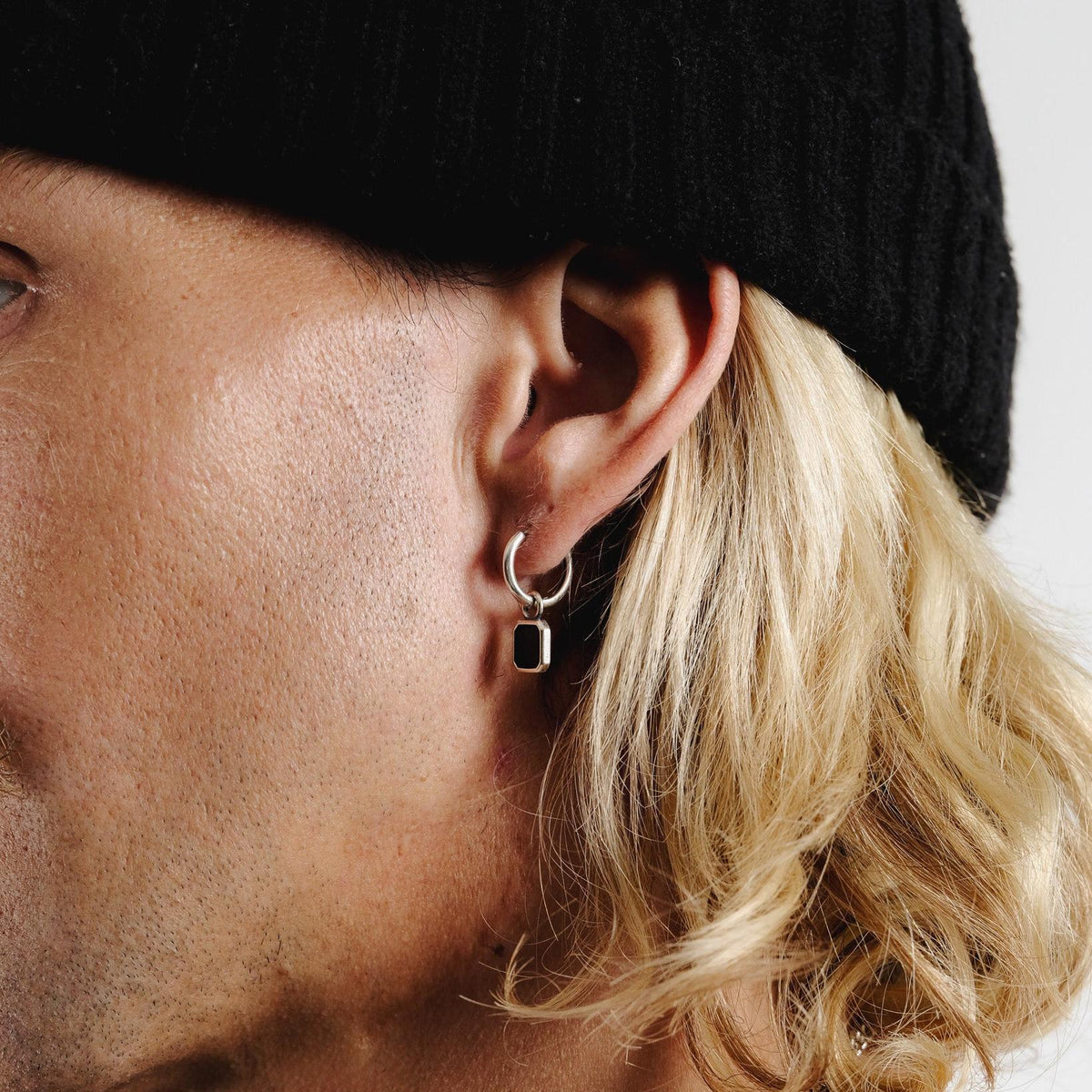 An editorial close-up of the Nox Earring by Billie Jo, worn by a male model, focusing on the sterling silver and black stone against his skin and hair.