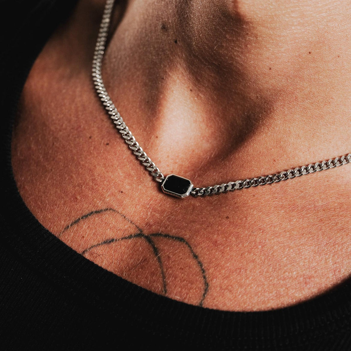 A close-up shot of the men's Eclipse Necklace in sterling silver, showing the black onyx stone and curb chain against the skin.