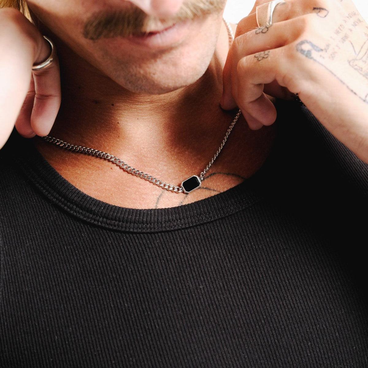 A man with a moustache adjusts the sterling silver Eclipse Necklace from Australian brand Billie Jo, showing the black onyx stone.