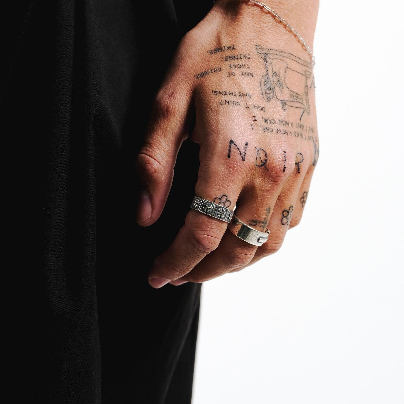 The Billie Jo Slim Link Bracelet in sterling silver, styled on a tattooed hand with rings for a modern, edgy look. A versatile piece of men's jewellery.