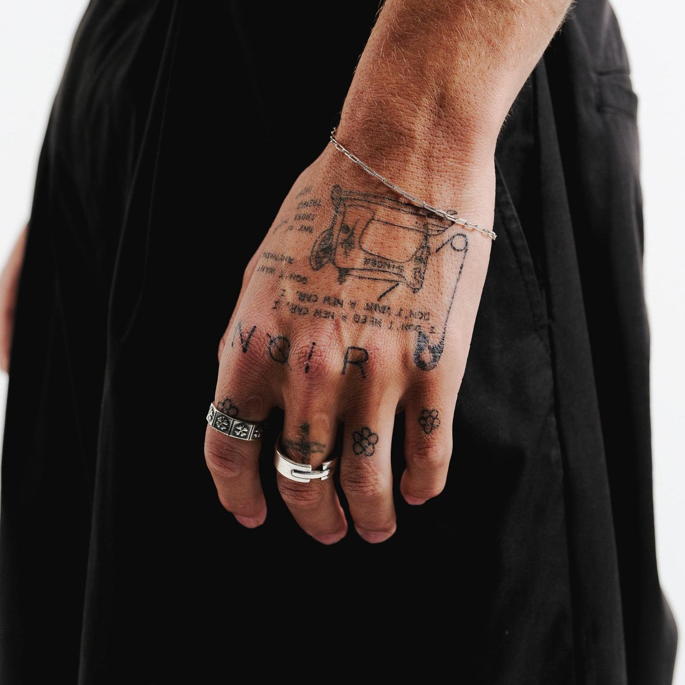 A close-up shot of a man's tattooed hand wearing the sterling silver Bind Ring by Billie Jo. The ring is styled with another silver ring, showcasing the brand's modern aesthetic.