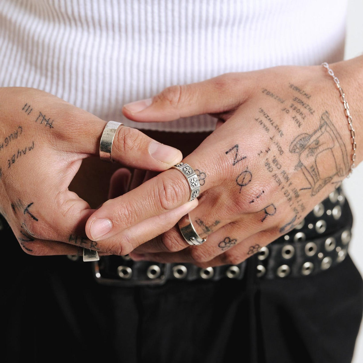 A man with tattooed hands wearing the sterling silver Billie Jo LUCKY RING, paired with a white ribbed tank top and a black leather belt.