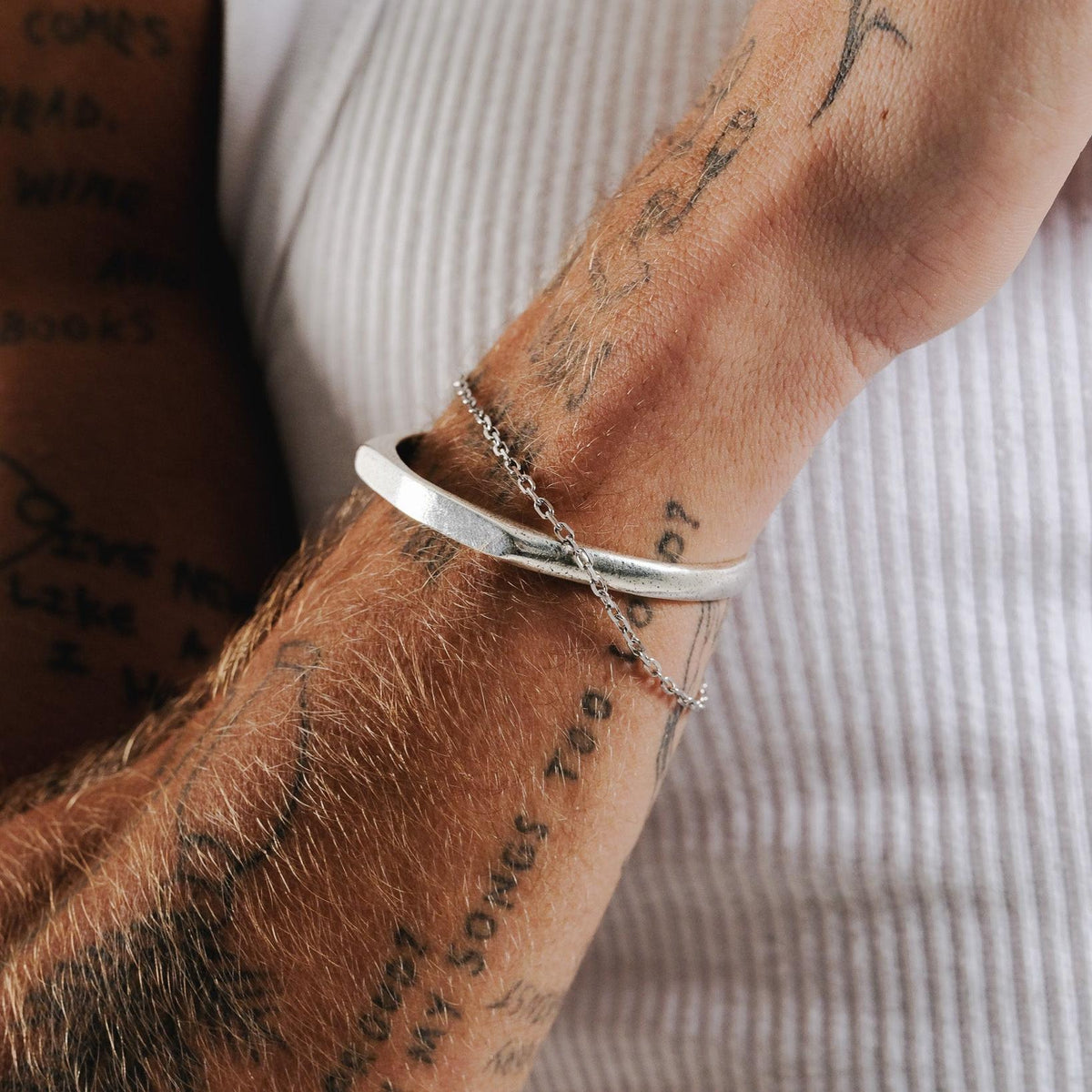 Close-up of the Billie Jo Slim Batch Bracelet on a man's tattooed arm, showing the fine chain detail against a silver cuff and white textured shirt.