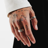 A tattooed hand wearing the sterling silver Elaris Ring from Billie Jo, showcasing its masculine and edgy style. A perfect addition to a ring stack.