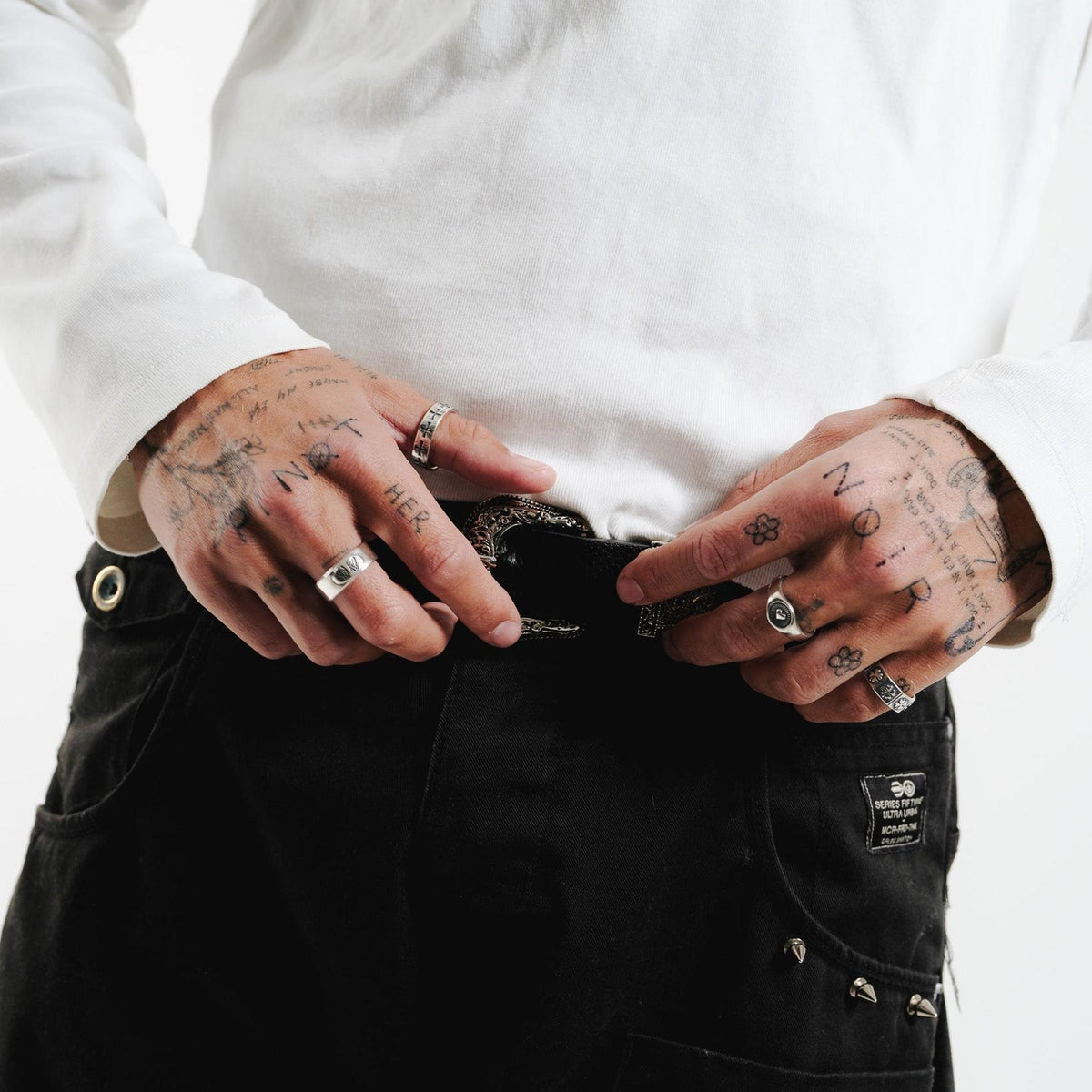 A close-up of a man's tattooed hands, wearing the sterling silver Vita Ring on his pinky finger. This shot for Billie Jo highlights the ring's versatility and how it can be stacked with other jewellery.