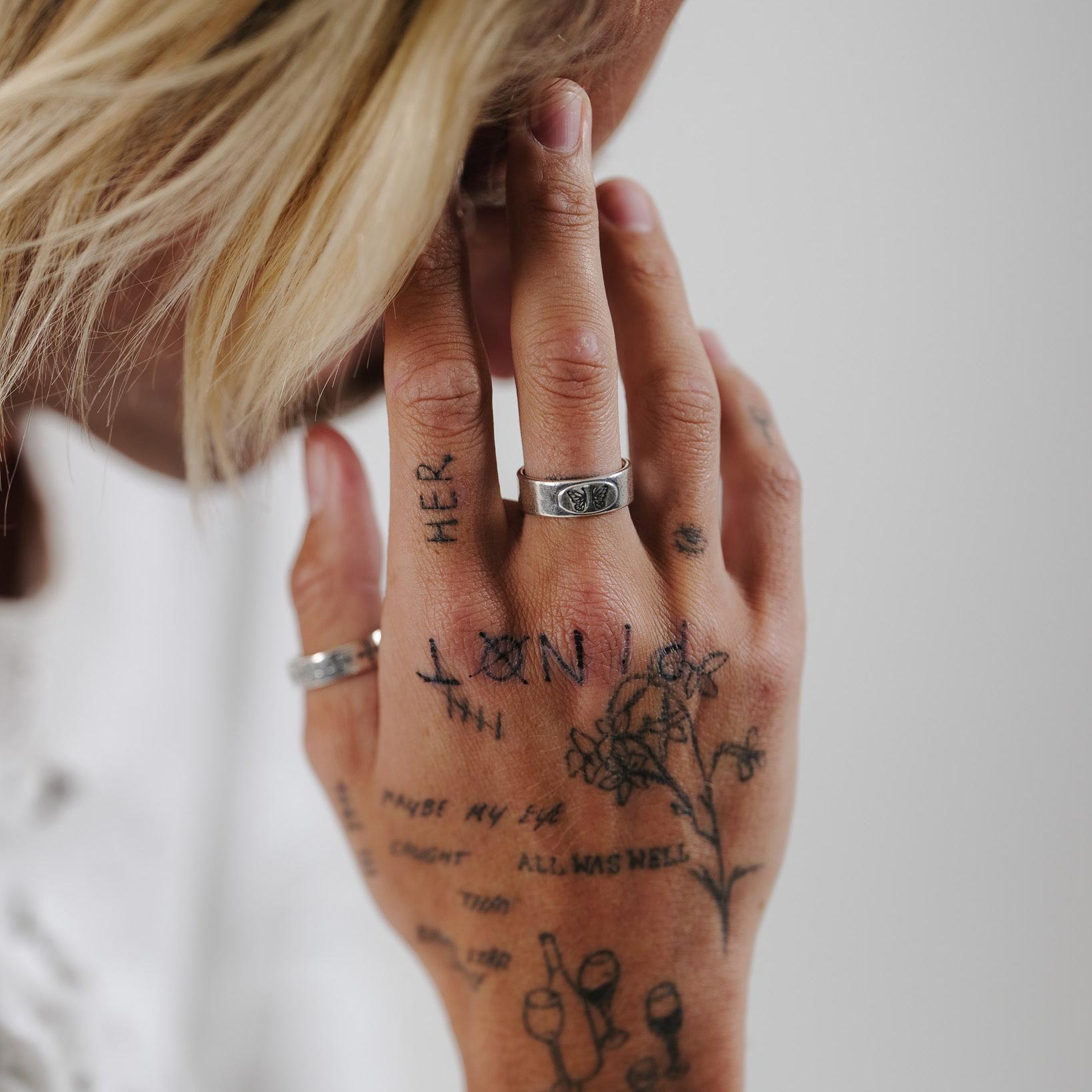 A model with blonde hair wears the Elaris Ring by Billie Jo, showing off the butterfly detail. An on-trend piece of men's jewellery from Australia.