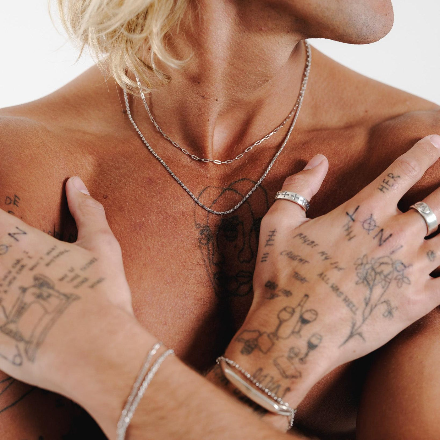 A model with tattooed hands wears the Billie Jo Sanctum Ring, styled with layered necklaces and bracelets. This editorial shot captures a modern, masculine aesthetic.