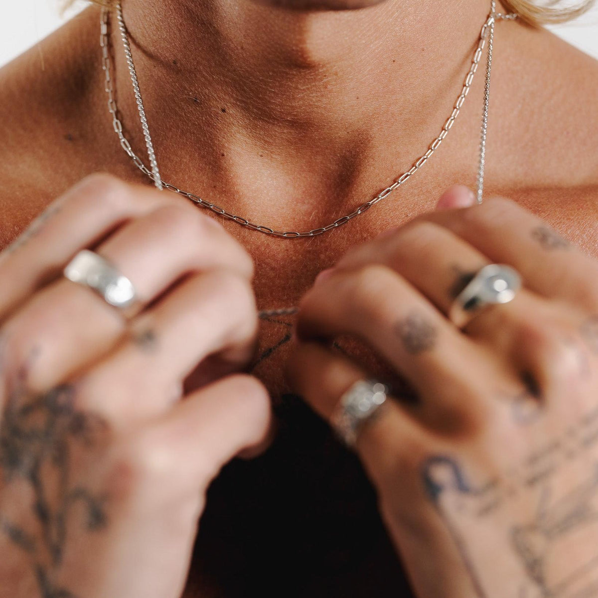 A close-up, artistic shot of the Billie Jo Slim Link Necklace in sterling silver, with a man's tattooed hands and chest blurred in the background.
