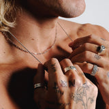 A man's tattooed hands adjusting the Billie Jo Slim Rope Necklace, showing the detail of the sterling silver chain and other rings for a complete jewellery look.