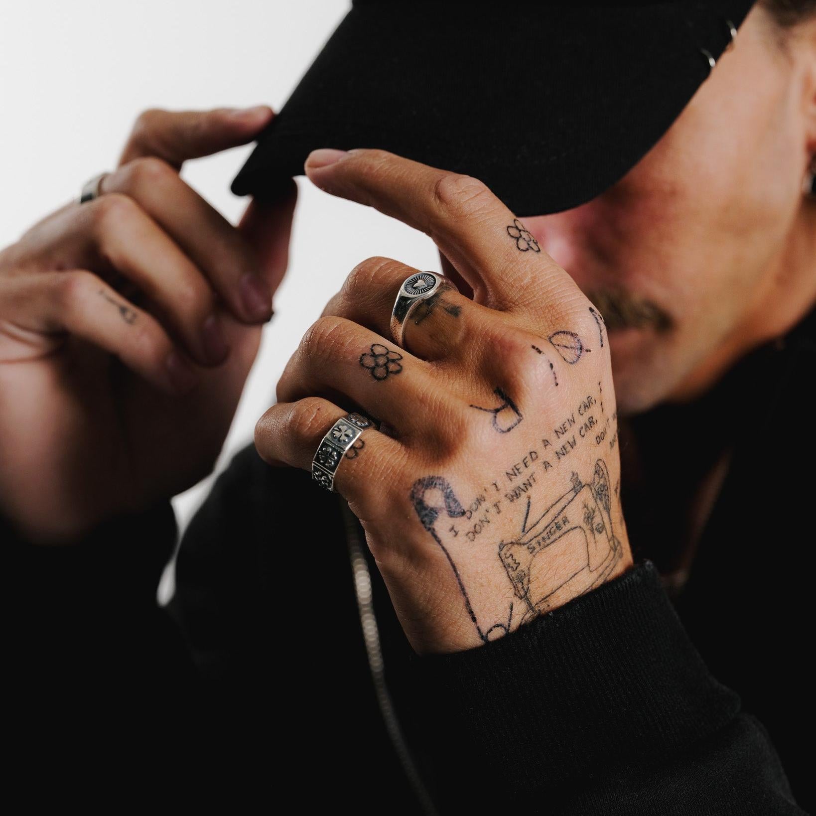 A man with hand tattoos wears the sterling silver Billie Jo LUCKY RING, styled with another silver ring and a black cap for a modern, edgy look.