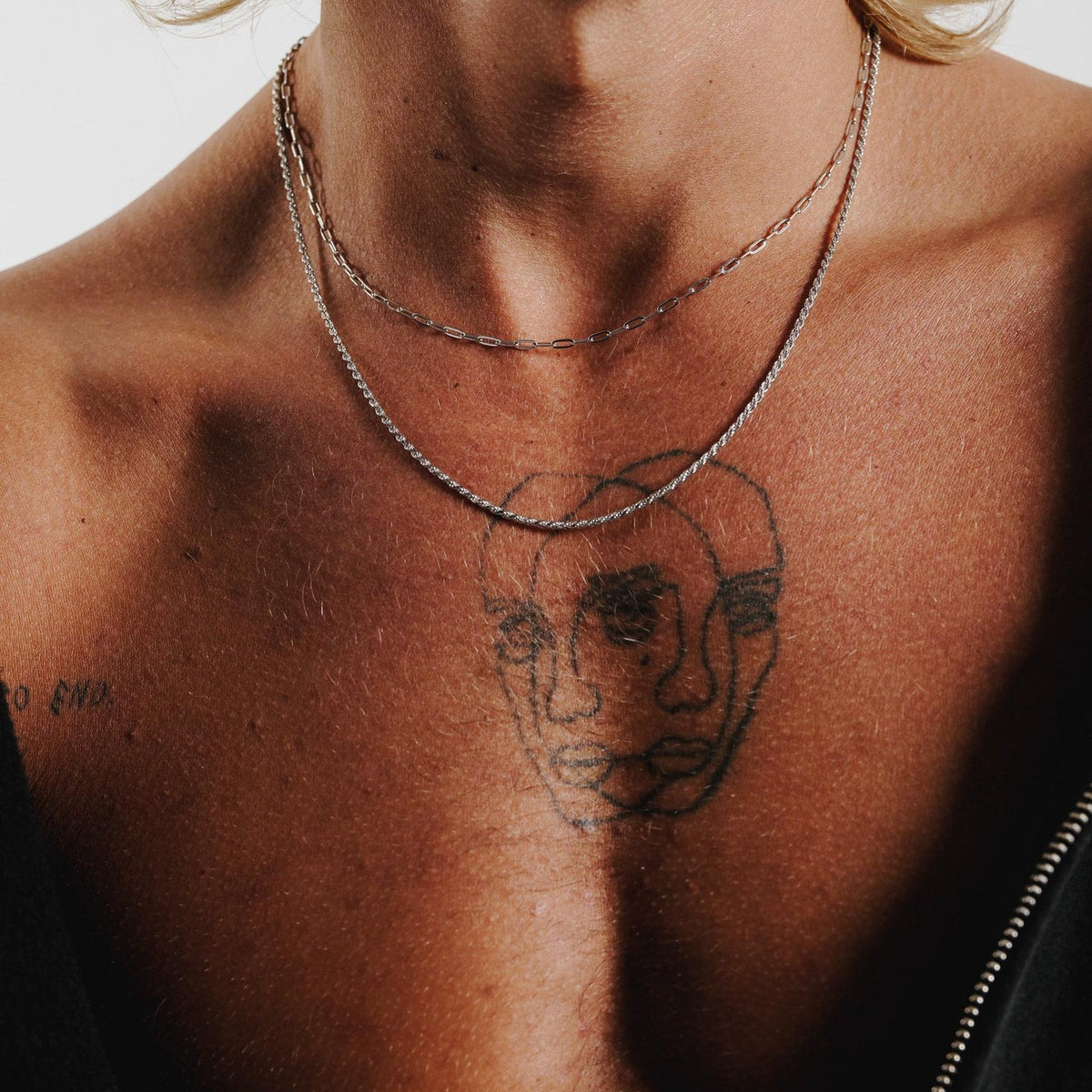 A detailed close-up of the sterling silver Slim Link Necklace from Billie Jo, resting on a man's chest with a tattoo visible underneath.