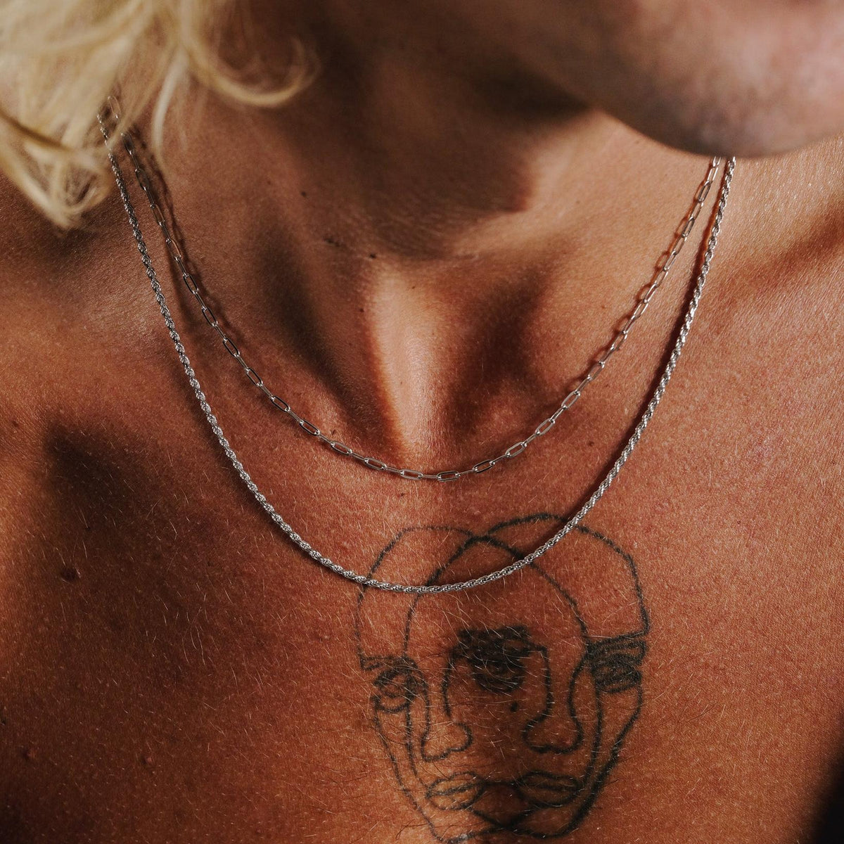 A close-up of the Billie Jo Slim Rope Necklace layered with another silver chain on a man's chest, showcasing its versatile styling for a modern look.