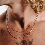 A close-up of the Billie Jo Slim Link Necklace in sterling silver, layered with a rope chain on a man's chest for a stylish, modern look.