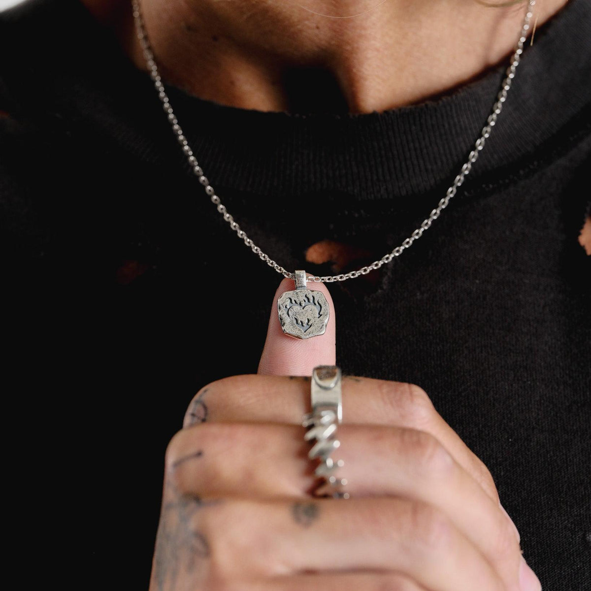 A detailed shot of the Ember Pendant held up to the camera, showing the intricate flame and heart design and the pendant's textured finish.