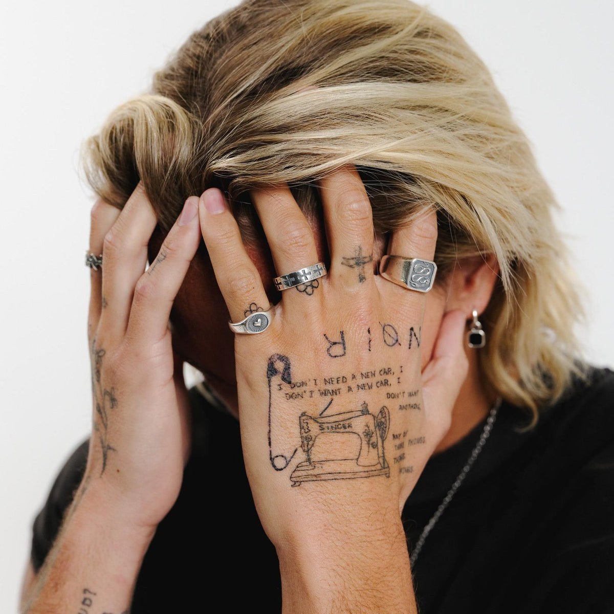 A model with blonde hair and tattooed hands, wearing the Billie Jo Sanctum Ring and other sterling silver jewellery. An editorial shot for this men's brand.