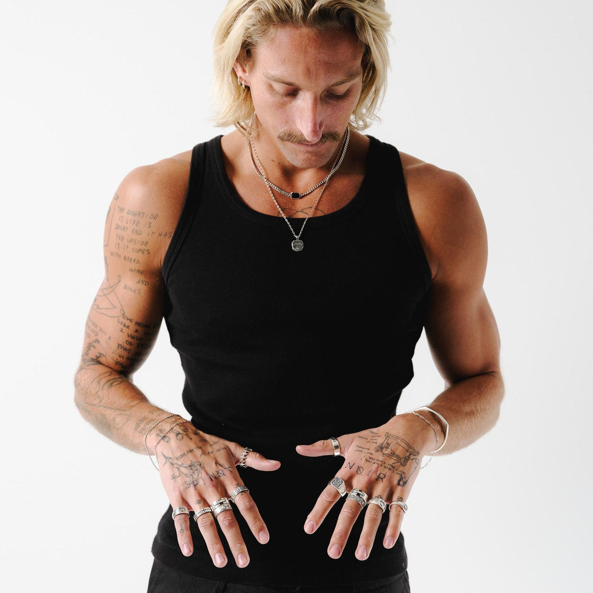 A model with tattoos wears the Ember Pendant layered with other silver necklaces, showcasing its versatility and style with a black tank top.