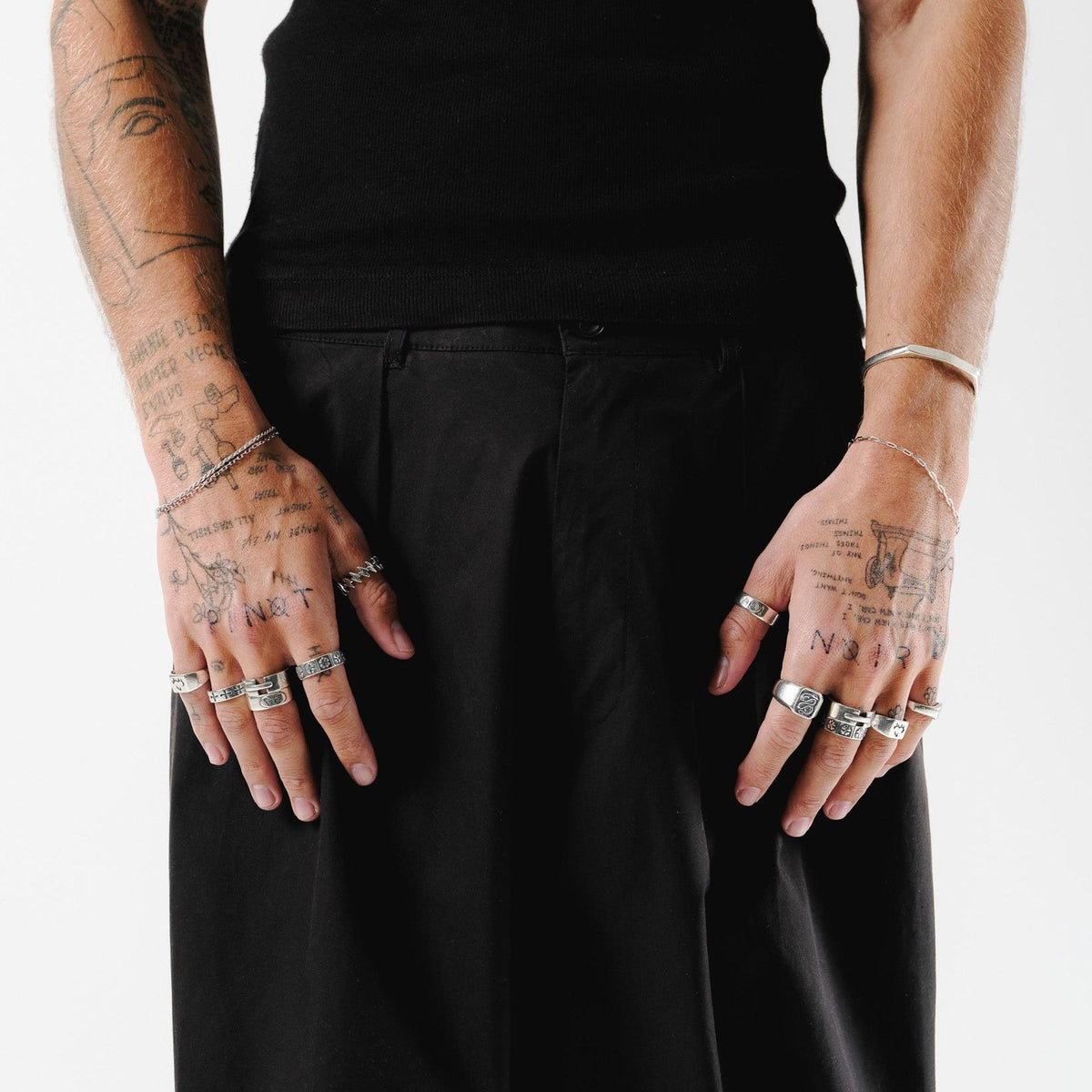 Editorial shot of a model with tattooed arms wearing two Billie Jo Slim Batch Bracelets, one on each wrist, styled with a black tank top and trousers.