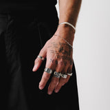 A man with tattooed hands wears the Billie Jo Slim Link Bracelet stacked with a silver cuff and multiple rings, showcasing a bold, layered jewellery look.
