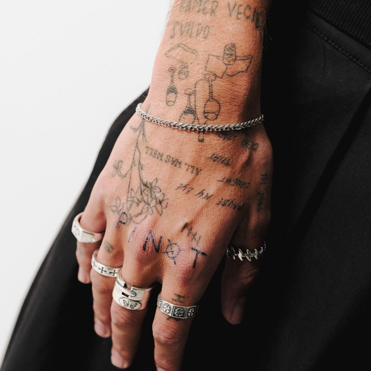 A tattooed man's hand adorned with a collection of sterling silver rings, including the Billie Jo LUCKY RING, against a black fabric background.