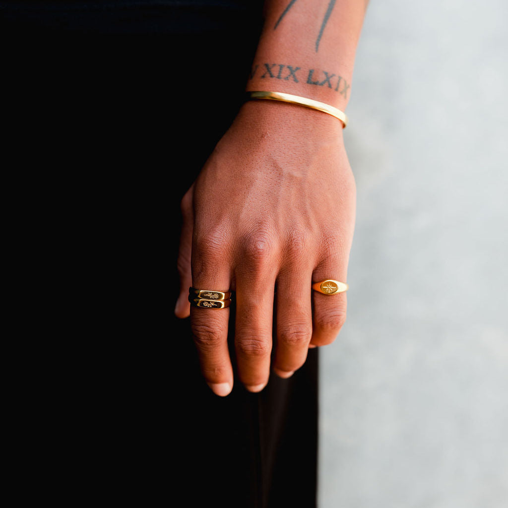 A close-up of a man's hand wearing the Billie Jo Rosa Stacker rings in gold, showing the detailed rose engraving and modern design of the jewellery.