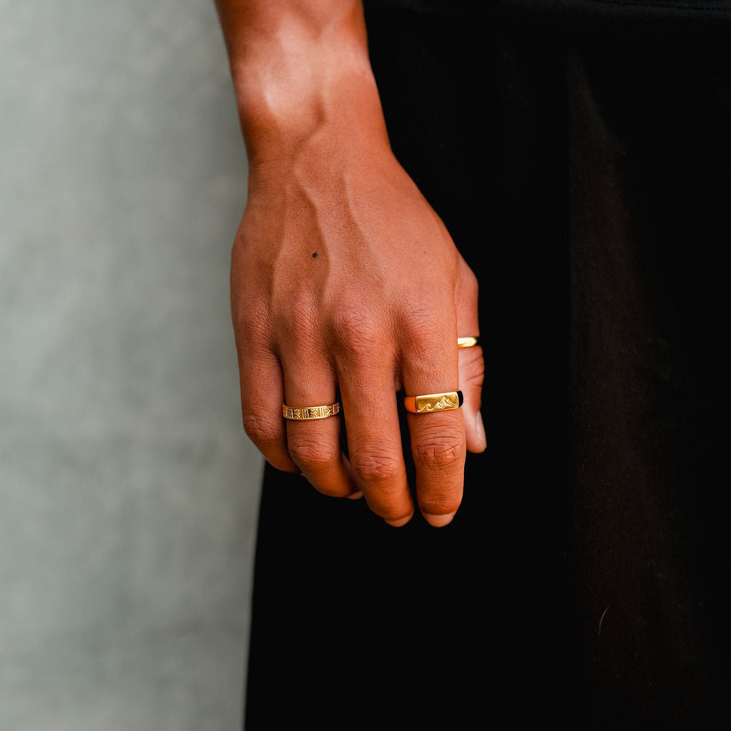The Billie Jo Union Ring in gold worn on a man's hand, styled with other rings against a simple background, highlighting the ring's design.
