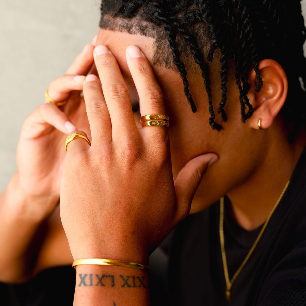 A man with braided hair wearing the gold Rosa Stacker rings by Billie Jo, paired with a gold cuff and necklace for a complete, modern jewellery look.