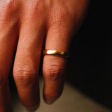A close-up of a man's hand wearing the Billie Jo gold stacker ring on his index finger. The simple, elegant design of the 18k gold vermeil ring contrasts with the dark background.
