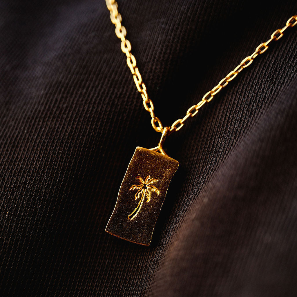 Angled close-up of the gold Paradiso Pendant by Billie Jo, highlighting the texture of the 18k gold vermeil and the engraved palm tree design.
