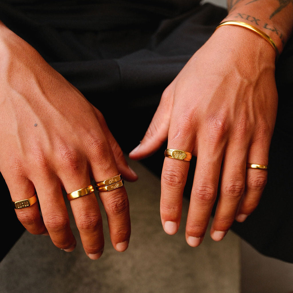 A detailed shot of a man's hands, showcasing a collection of gold rings from Australian brand Billie Jo. The Stacker Ring is featured amongst other designs, creating a personalised look.