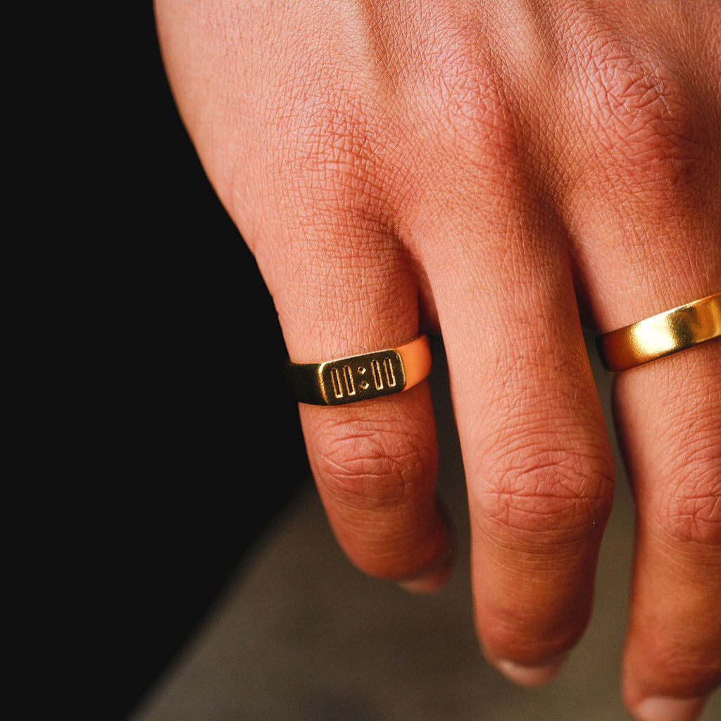 A close-up of the Billie Jo Momento Ring in gold, worn on a man's finger against a dark background, highlighting the '00:00' engraving. Modern Australian men's jewellery.