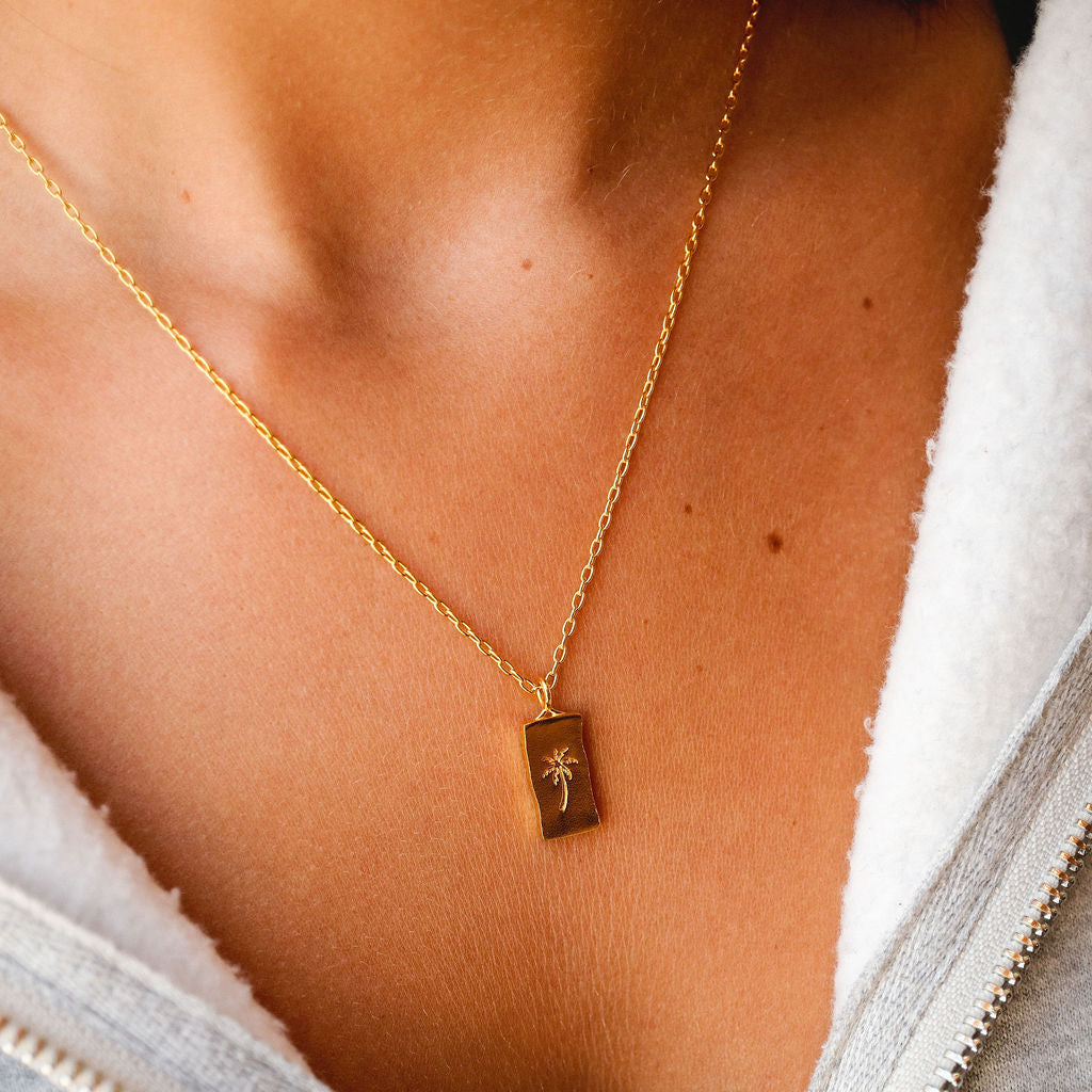 On-person shot of the Billie Jo Paradiso Pendant in gold, worn with a casual grey zip-up hoodie, showing how it sits on the collarbone.
