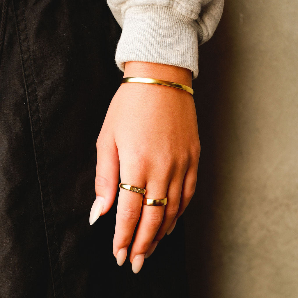 A man's hand with the gold Rosa II Ring, showing how it can be stacked with other rings and a gold cuff for a complete jewellery look.