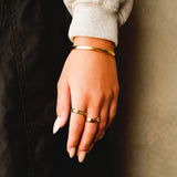 A man's hand with the gold Rosa II Ring, showing how it can be stacked with other rings and a gold cuff for a complete jewellery look.