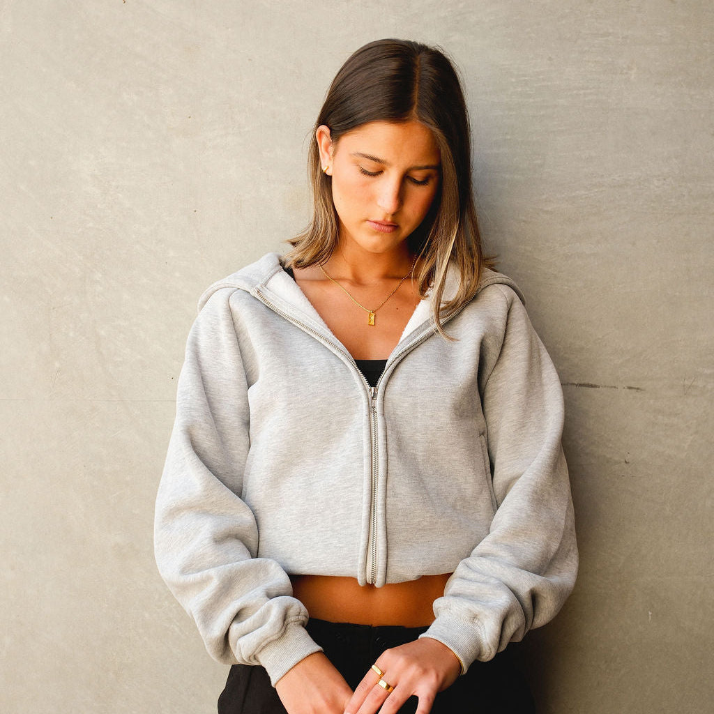 A female model looking down, wearing the gold Paradiso Pendant by Billie Jo with a grey zip hoodie. A versatile piece of Australian men's jewellery.