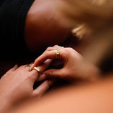 A close-up lifestyle image showing a man wearing the Billie Jo Rosa II Ring in gold, with a soft, artistic focus on the hands and jewellery.