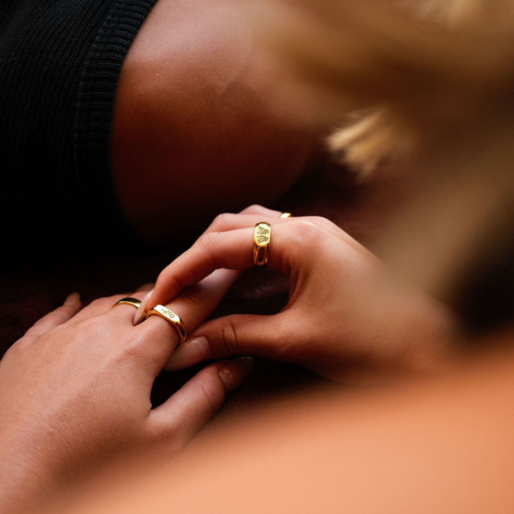 A close-up lifestyle image showing a man wearing the Billie Jo Rosa II Ring in gold, with a soft, artistic focus on the hands and jewellery.