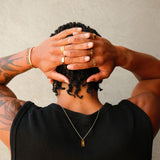A man with his hands behind his head, showing off a collection of Billie Jo gold rings, including the Serenity Ring, and a gold cuff.