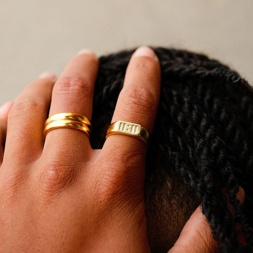 A close-up of the Billie Jo Momento Ring worn on a man's hand, with his fingers resting on his braided hair, showing the ring's texture and colour.