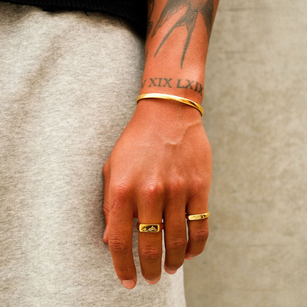 The Drifter Cuff in gold by Billie Jo, shown on a man's wrist against a textured background, highlighting the cuff's polished finish.