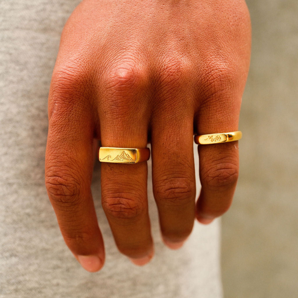 A close-up on-hand shot of a man wearing the Billie Jo Rosa II Ring in gold, featuring a detailed engraving, paired with another gold band.
