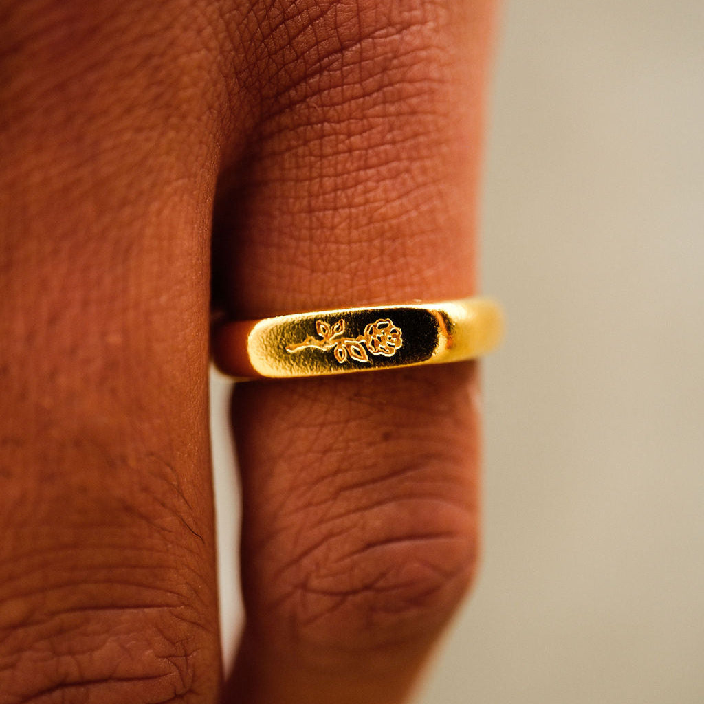A macro shot of the Billie Jo Rosa II Ring in gold, highlighting the intricate rose engraving on the signet face. A unique men's jewellery piece.