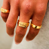 A man's hand wearing the gold Serenity Ring from Billie Jo, styled with other gold rings for a layered, contemporary look.