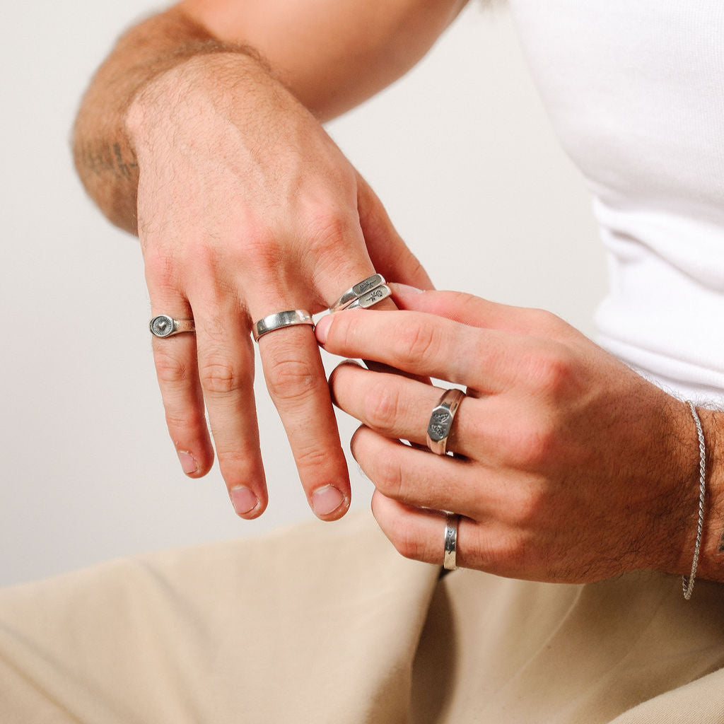 A man's hands adjusting his rings, wearing the Revival Ring and other pieces from Billie Jo, showcasing a styled look for the modern man.