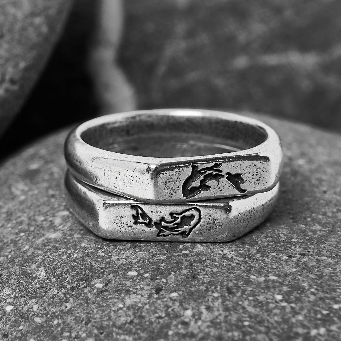 Two sterling silver KOI I Rings from Billie Jo are stacked on a textured rock, shot in black and white to highlight the engraved koi fish design.