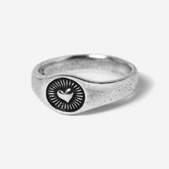 A 45-degree product shot of the sterling silver Vita Ring by Billie Jo. The signet-style ring features a central heart emblem with radiating sunbeam engravings, showcasing its textured, oxidised finish.