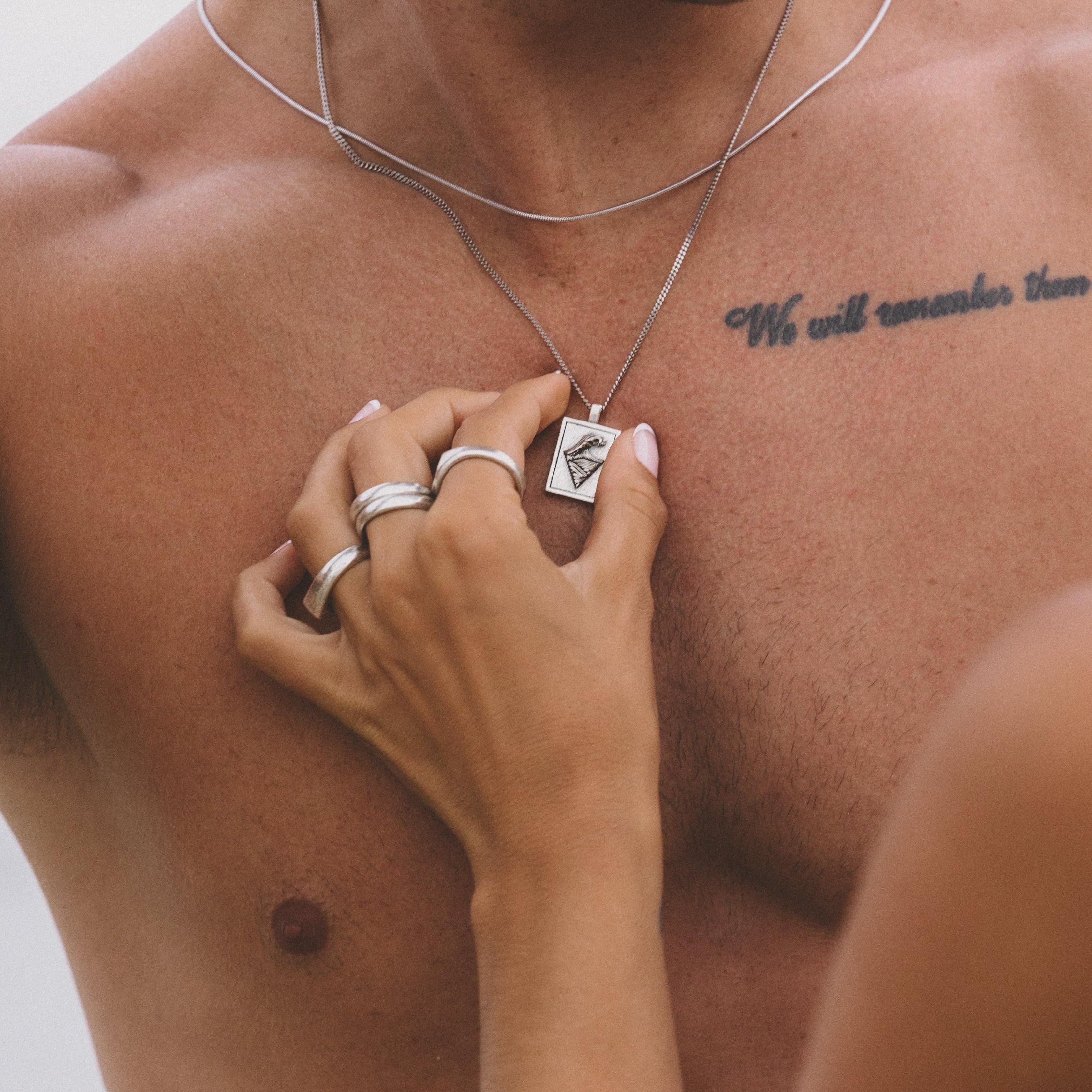 A close-up lifestyle image of the Billie Jo Burleigh Pendant on a man's chest, with a soft, natural light highlighting the silver and the wave design.