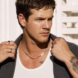 A male model wearing the Billie Jo ONYX 2.0 RING and a silver chain necklace, with a white tank top and dark jacket. He is looking to the side with a serious expression.