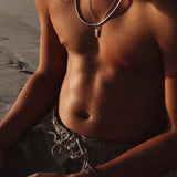 A close-up lifestyle shot of a man's torso on the beach, wearing the sterling silver Paradiso Pendant from Billie Jo with a silver chain.